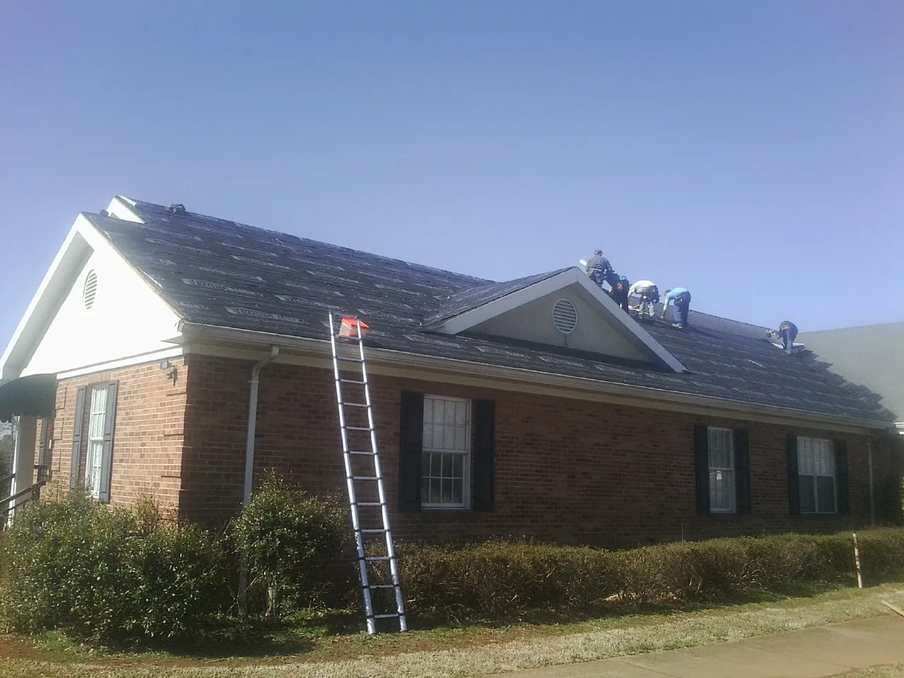 Crew tearing shingles off a brick ranch roof with a ladder set — Emergency Roof Repair work by our crew in Orient