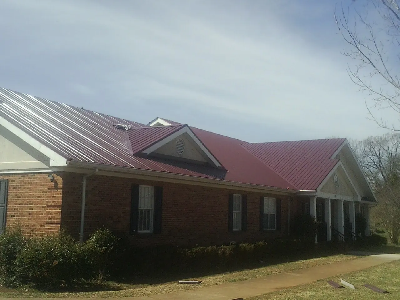Red metal roof with gabled entries on a long brick building, from a Hail Damage Roof Repair job in Orient