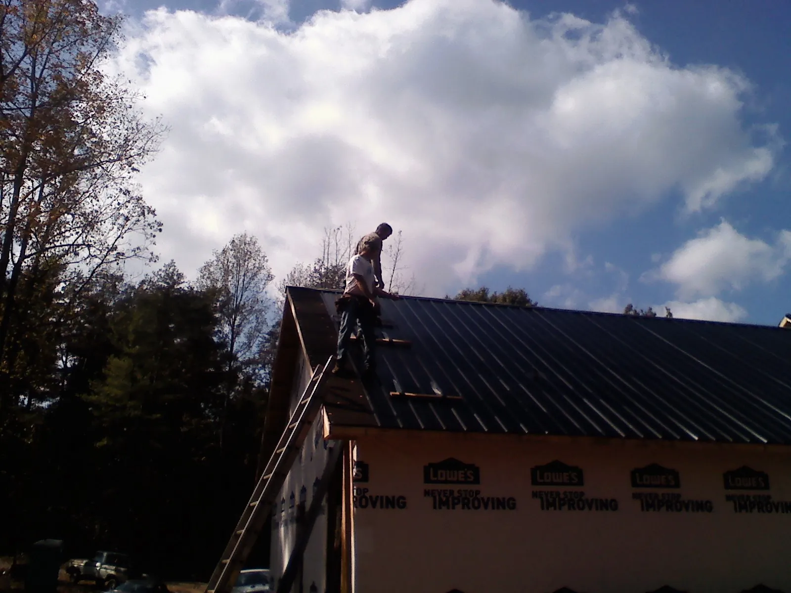 Roofer fastening dark metal panels high against a cloudy sky, from a Roof Inspection job in Orient